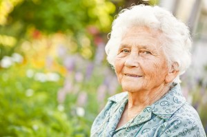 Elderly woman smiling gently in a sunlit garden.